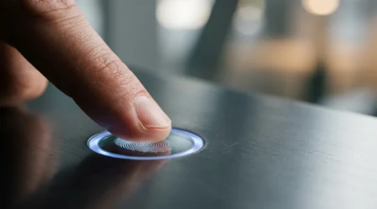Gros plan d'une main positionnant son pouce sur un capteur d'empreinte digitale moderne dans un environnement minimaliste et épuré